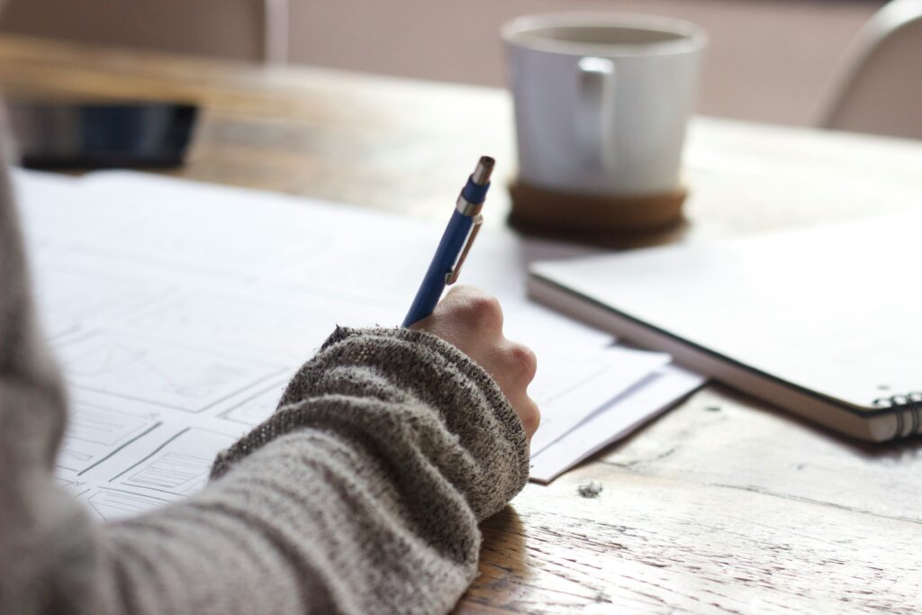 unseen-studio-s9CC2SKySJM-unsplash A person writing on a stack of papers on a desk with a mug